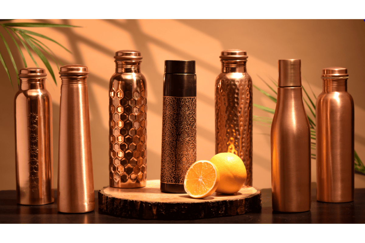 Set of copper water bottles on a wooden stand with fruits in the background